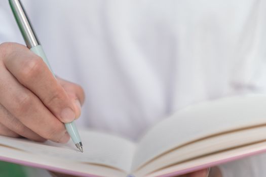 Woman hand writing down in small white memo notebook for take a note not to forget or to do list plan for future.