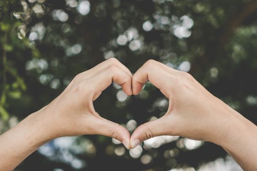 Woman hand do heart shape on green nature bokeh tropical background.