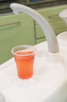 Closeup detail of orange mouthwash drink and faucet in dentists surgery