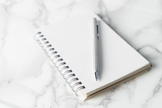 Silver metal pen on blank notebook page on marble desk