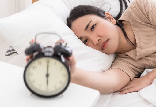 Asian woman on bed reaching out to stop the alarm clock