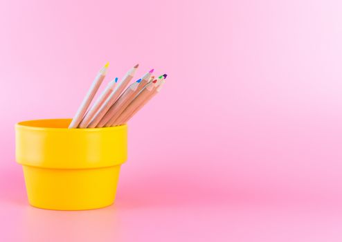 Color Pencil in orange bucket on pink background copy space