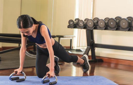 Strong asian woman is doing a plank in a fitness gym