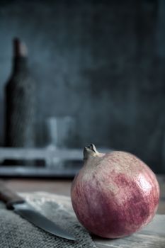 On the kitchen table on the cutting Board is a large ripe pomegranate fruit. Next to it is a kitchen knife. A dark background and copy space.