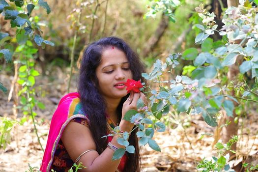 A young girl holding a rose in the garden and looking at red rose flower