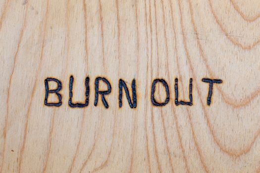 the words burn out handwritten with woodburner on flat plywood surface.