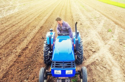 A farmer on a tractor cultivates a farm field. Soil milling, crumbling and mixing. Preparatory work for a new planting. Loosening surface, cultivating land for further planting. Agroindustry, farming.