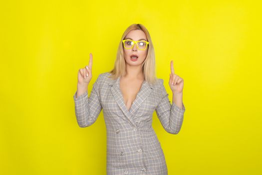 Attractive blonde woman in plaid jacket dress over yellow background wearing yellow glasses