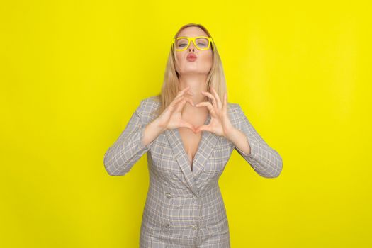 Attractive blonde woman in plaid jacket dress over yellow background wearing yellow glasses