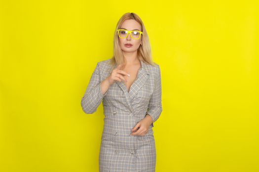 Attractive blonde woman in plaid jacket dress over yellow background wearing yellow glasses