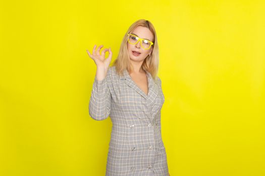 Attractive blonde woman in plaid jacket dress over yellow background wearing yellow glasses