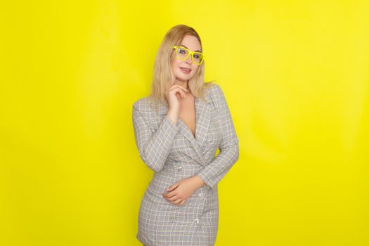 Attractive blonde woman in plaid jacket dress over yellow background wearing yellow glasses