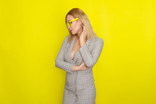 Attractive blonde woman in plaid jacket dress over yellow background wearing yellow glasses