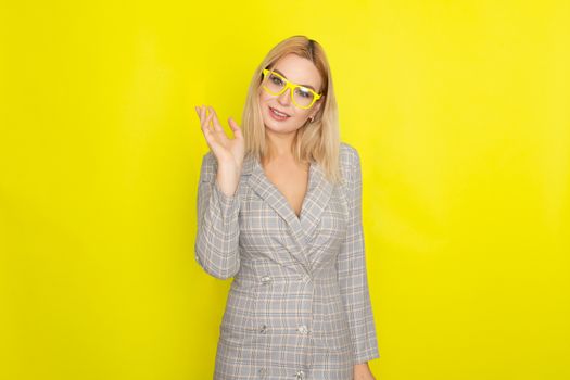 Attractive blonde woman in plaid jacket dress over yellow background wearing yellow glasses