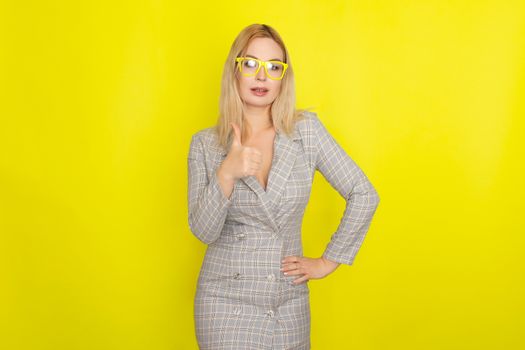 Attractive blonde woman in plaid jacket dress over yellow background wearing yellow glasses