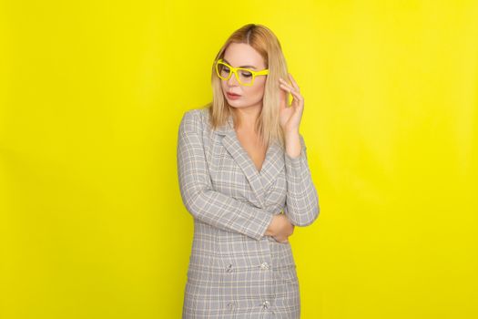 Attractive blonde woman in plaid jacket dress over yellow background wearing yellow glasses