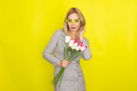 Blonde woman in plaid dress holding tulips bouquet over yellow background