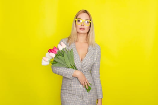 Blonde woman in plaid dress holding tulips bouquet over yellow background