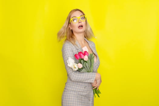 Blonde woman in plaid dress holding tulips bouquet over yellow background