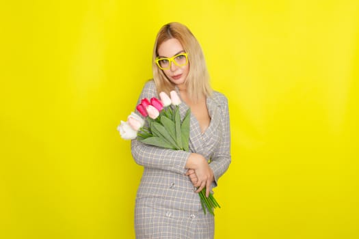 Blonde woman in plaid dress holding tulips bouquet over yellow background