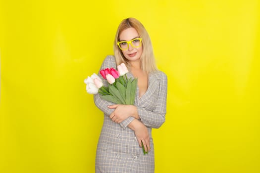 Blonde woman in plaid dress holding tulips bouquet over yellow background
