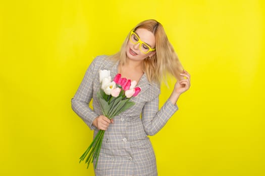 Blonde woman in plaid dress holding tulips bouquet over yellow background