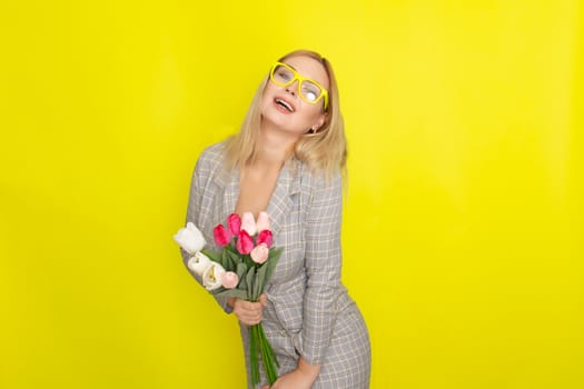 Blonde woman in plaid dress holding tulips bouquet over yellow background