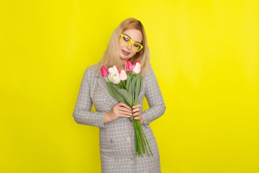 Blonde woman in plaid dress holding tulips bouquet over yellow background