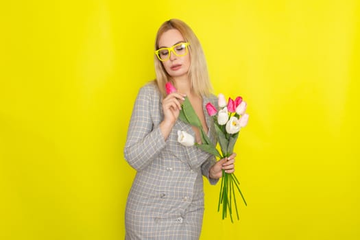 Blonde woman in plaid dress holding tulips bouquet over yellow background