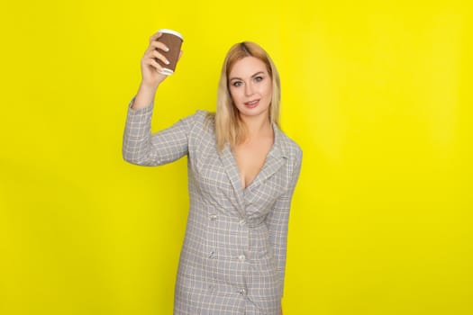 Business blonde woman wearing plaid jacket style dress and drinking coffee over yellow background