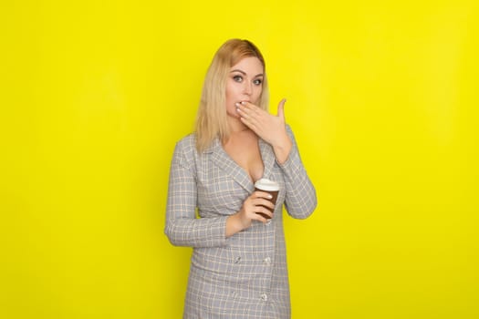 Business blonde woman wearing plaid jacket style dress and drinking coffee over yellow background