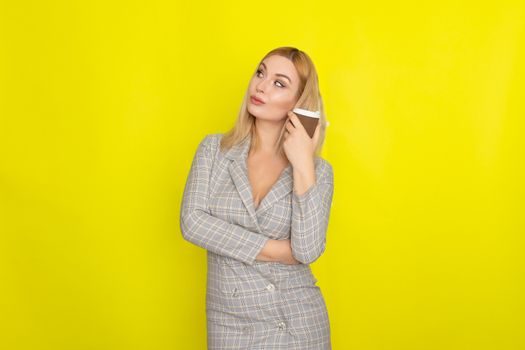 Business blonde woman wearing plaid jacket style dress and drinking coffee over yellow background