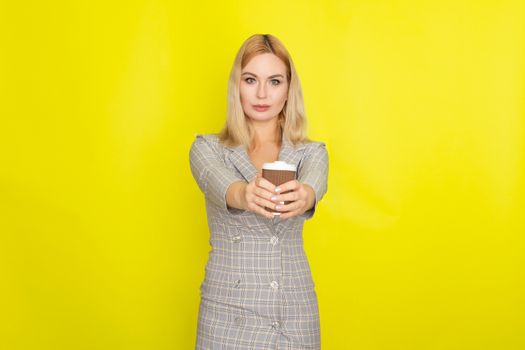 Business blonde woman wearing plaid jacket style dress and drinking coffee over yellow background