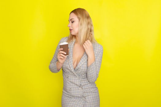 Business blonde woman wearing plaid jacket style dress and drinking coffee over yellow background