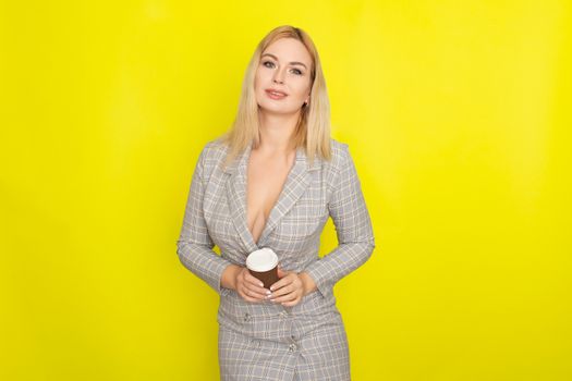 Business blonde woman wearing plaid jacket style dress and drinking coffee over yellow background