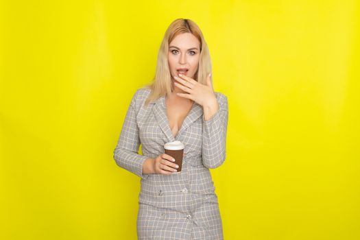 Business blonde woman wearing plaid jacket style dress and drinking coffee over yellow background