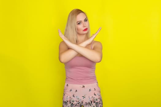 Indoor summer closeup portrait of young stylish fashion glamorous blonde woman posing in pink shorts and shirt, standing over yellow background