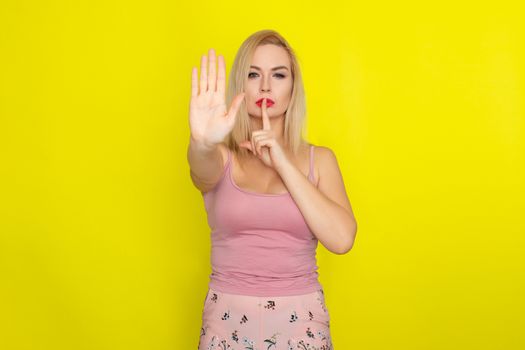 Indoor summer closeup portrait of young stylish fashion glamorous blonde woman posing in pink shorts and shirt, standing over yellow background