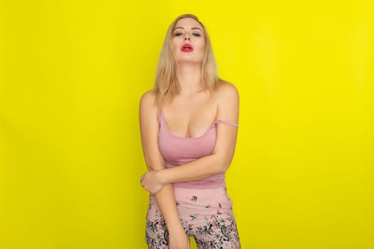 Indoor summer closeup portrait of young stylish fashion glamorous blonde woman posing in pink shorts and shirt, standing over yellow background