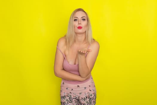 Indoor summer closeup portrait of young stylish fashion glamorous blonde woman posing in pink shorts and shirt, standing over yellow background