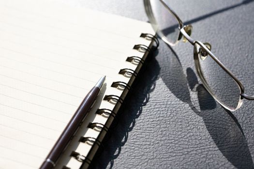 Pen on spiral notebook near spectacles on black table