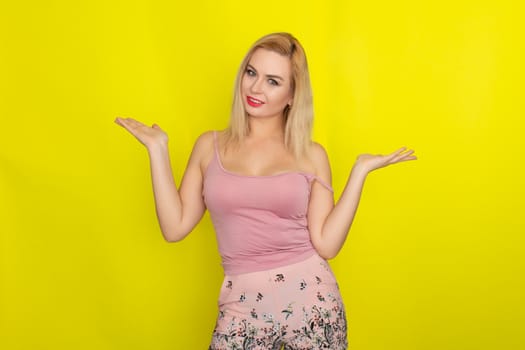 Indoor summer closeup portrait of young stylish fashion glamorous blonde woman posing in pink shorts and shirt, standing over yellow background