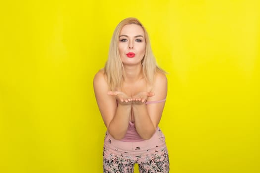 Indoor summer closeup portrait of young stylish fashion glamorous blonde woman posing in pink shorts and shirt, standing over yellow background