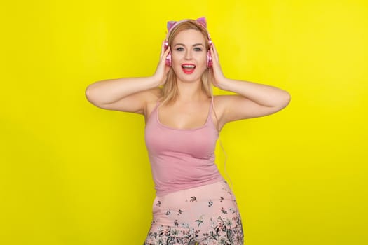 Blonde woman in pink summer clothing wearing pink headphones like kitten ears