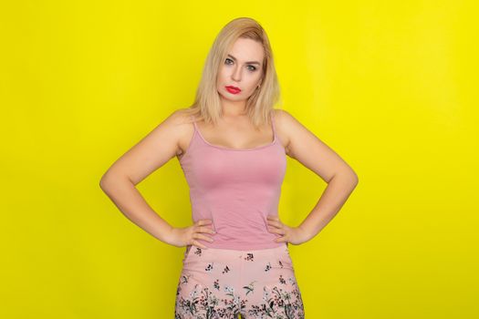 Indoor summer closeup portrait of young stylish fashion glamorous blonde woman posing in pink shorts and shirt, standing over yellow background