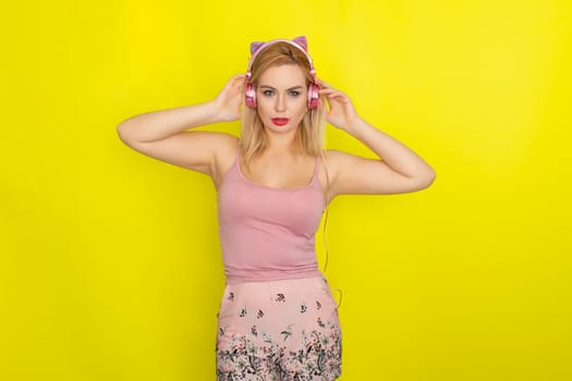 Blonde woman in pink summer clothing wearing pink headphones like kitten ears