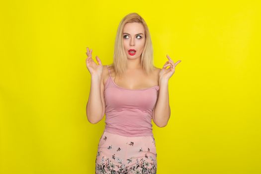 Indoor summer closeup portrait of young stylish fashion glamorous blonde woman posing in pink shorts and shirt, standing over yellow background