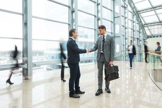 Business people shaking hands standing in a crowd of walking people