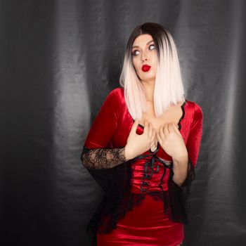 Portrait of a young blonde woman in a red vampire costume on a black background in the studio