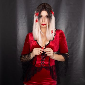 Young beautiful blonde woman in a red vampire dress on a black background. She has a lot of red little spiders
